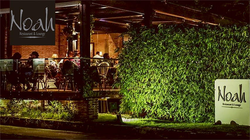 Exterior view of Noah Restaurant & Lounge with outdoor seating and greenery.